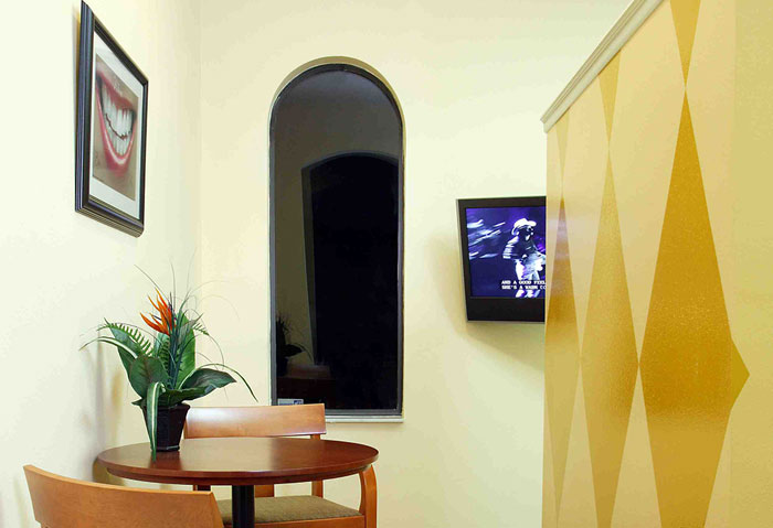 An interior view of a clean, modern hotel room with a yellow accent wall, a flat-screen TV mounted on the wall, and a dining table with chairs.